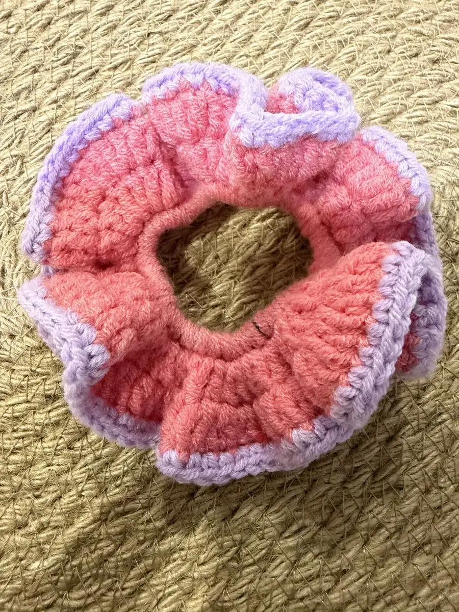A handmade ruffle scrunchie in coral pink with a lilac edge.