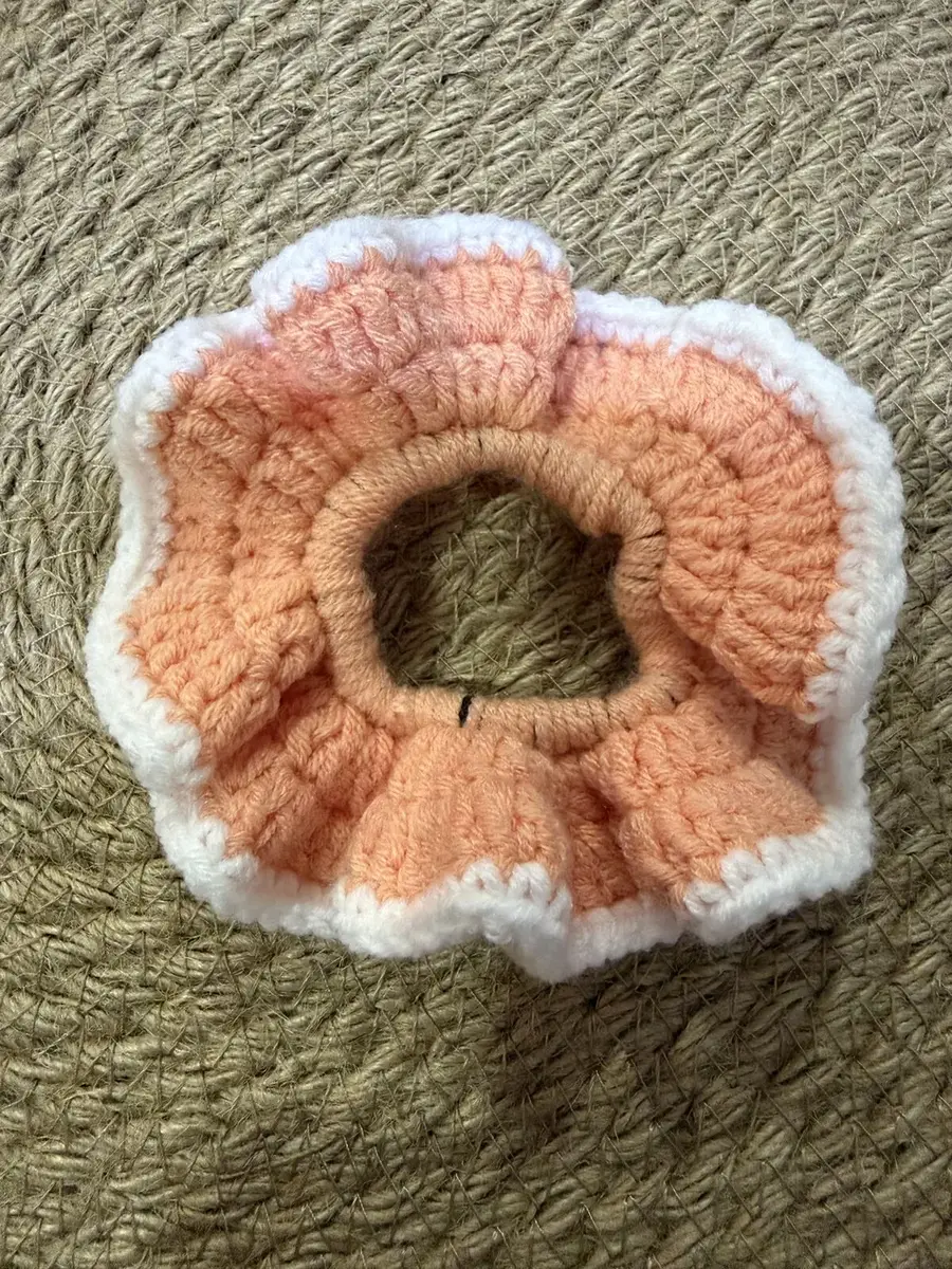 A handmade ruffle scrunchie in peach with a white edge.