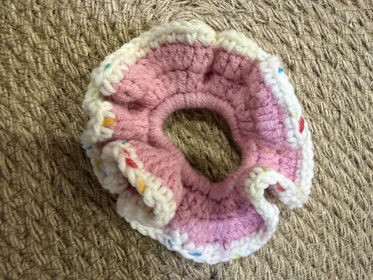 A handmade ruffle scrunchie in pink with a white confetti edge.