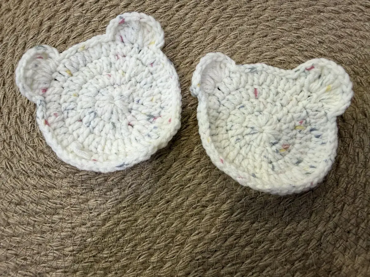 Two cream confetti bear-head coasters.