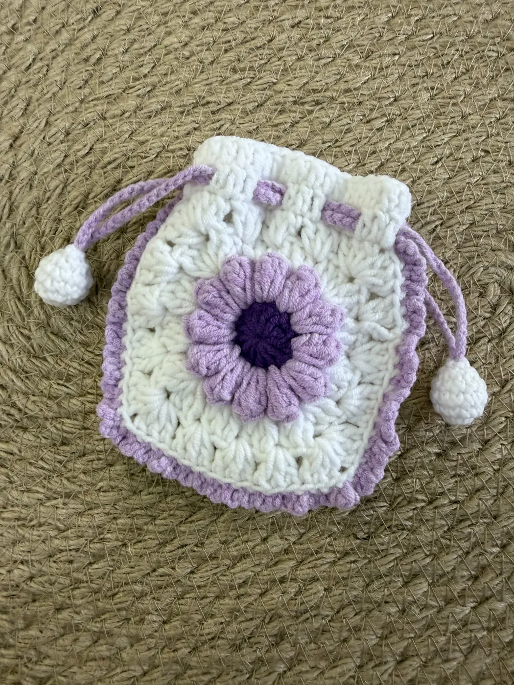 A lavender and white crochet drawstring pouch with a flower.