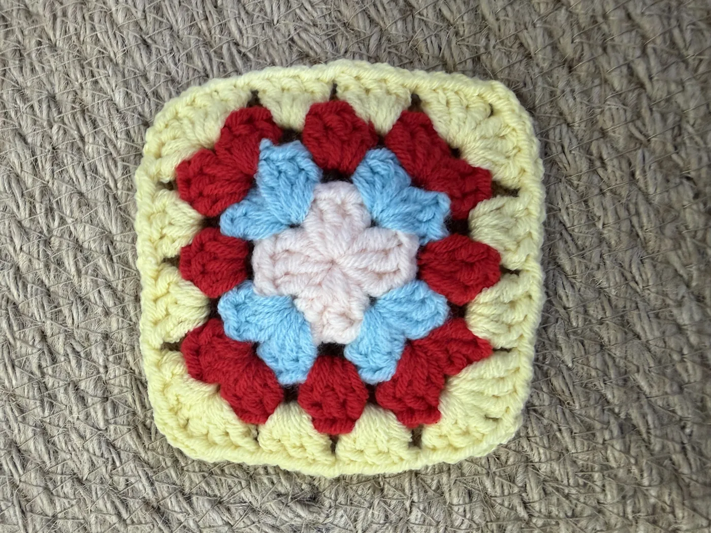 A crochet granny square in red, yellow and cream.