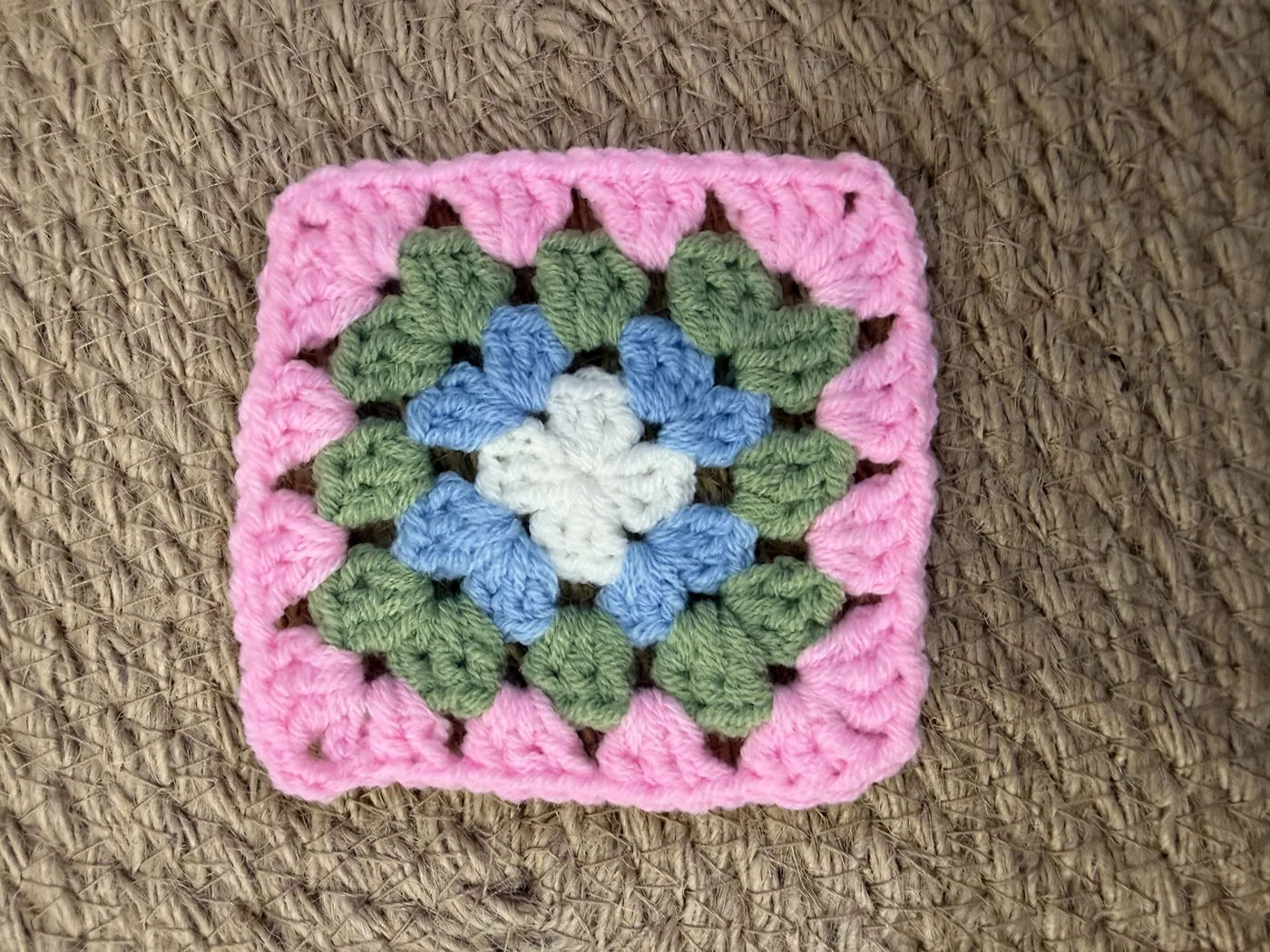 A crochet granny square in pink, green, blue and yellow.