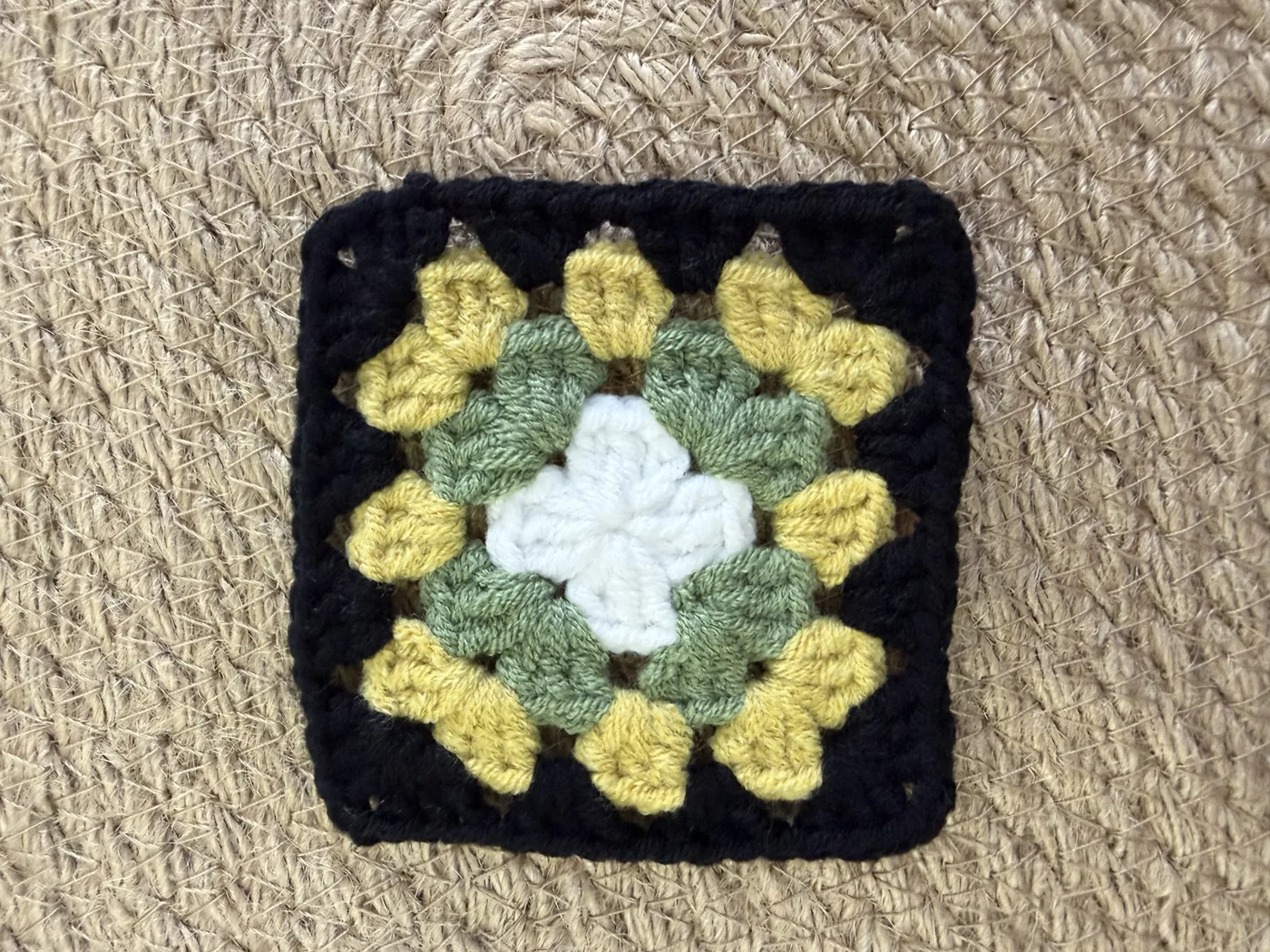 A crochet granny square with a black border and a yellow centre.