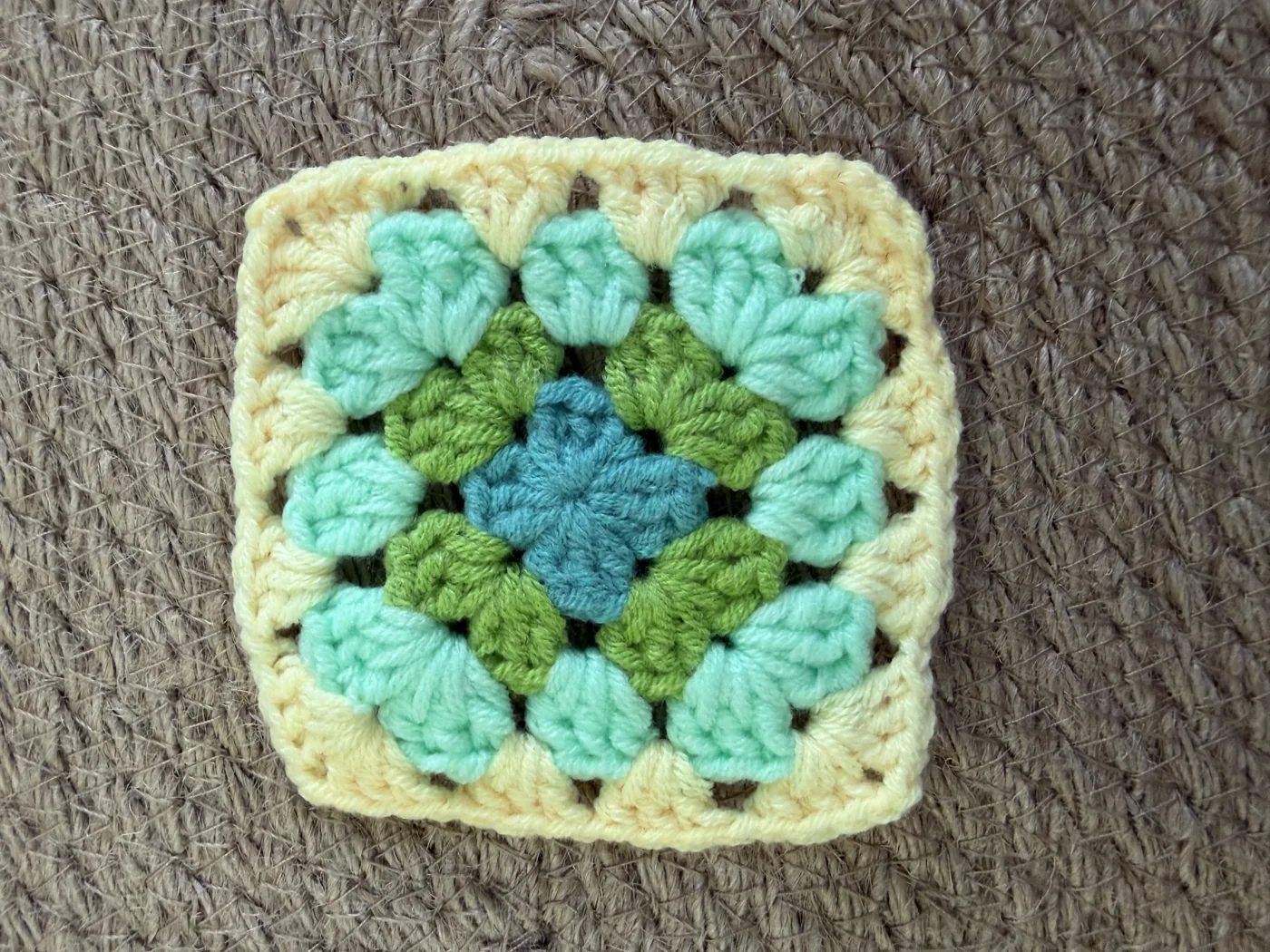 A crochet granny square in mint, yellow and blue.